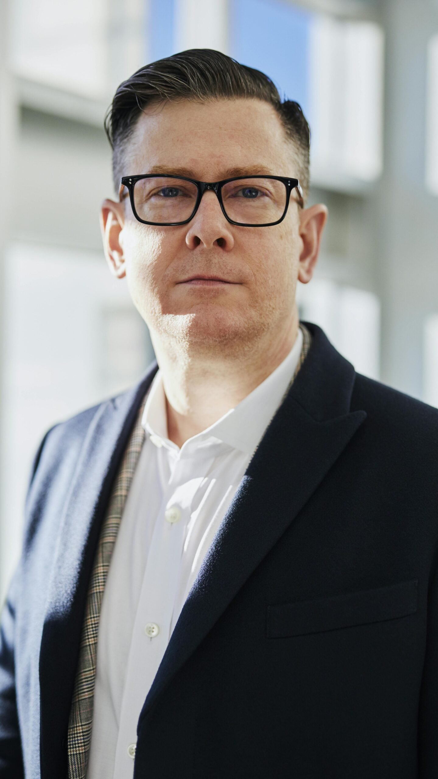 Profile portrait of a confident business executive wearing eyeglasses in a sunlit office setting.