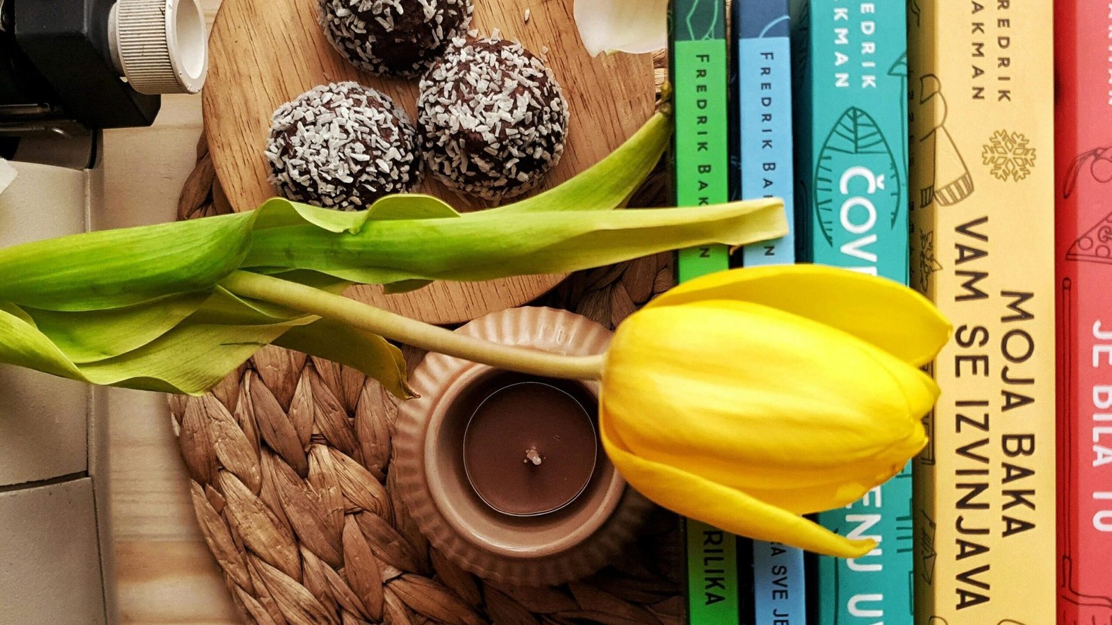Top view stack of books on table near beautiful yellow tulip and orchid flowers arranged with chocolate truffles placed on wicker placemat